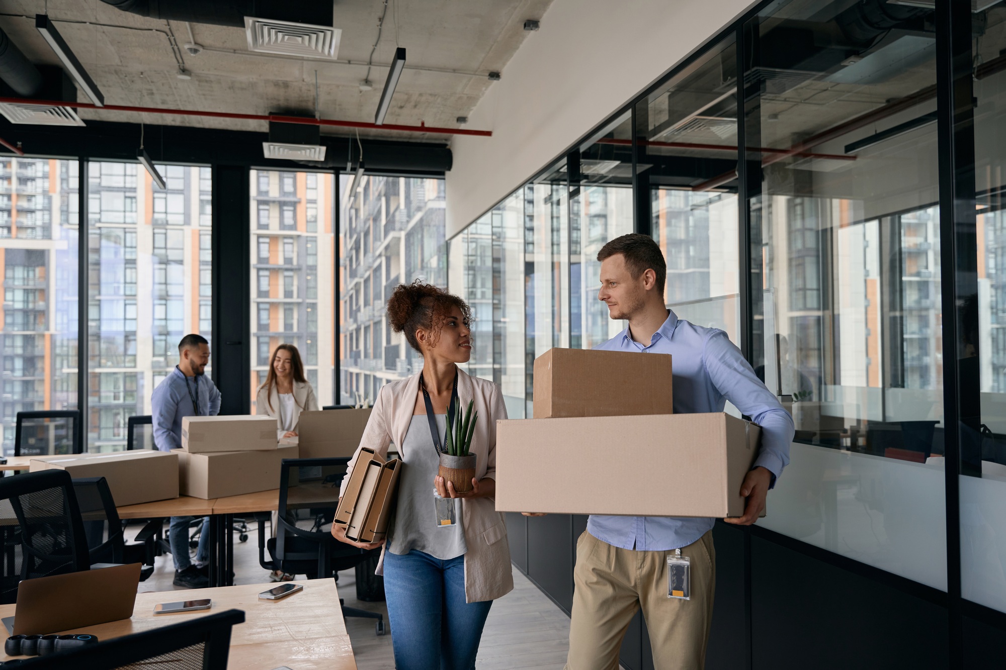 Deux collègues dans un bureau moderne emballent des cartons à déménager, échanges amicaux et casiers prêts. commentaire: comment bien organiser son déménagement en 1 mois.